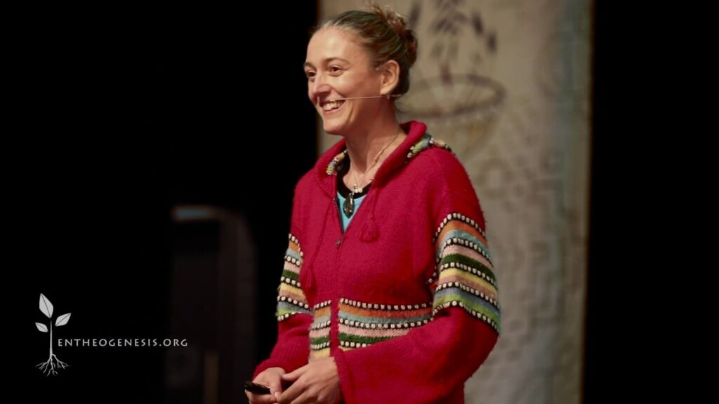 A woman in a red sweater smiles while holding a microphone.