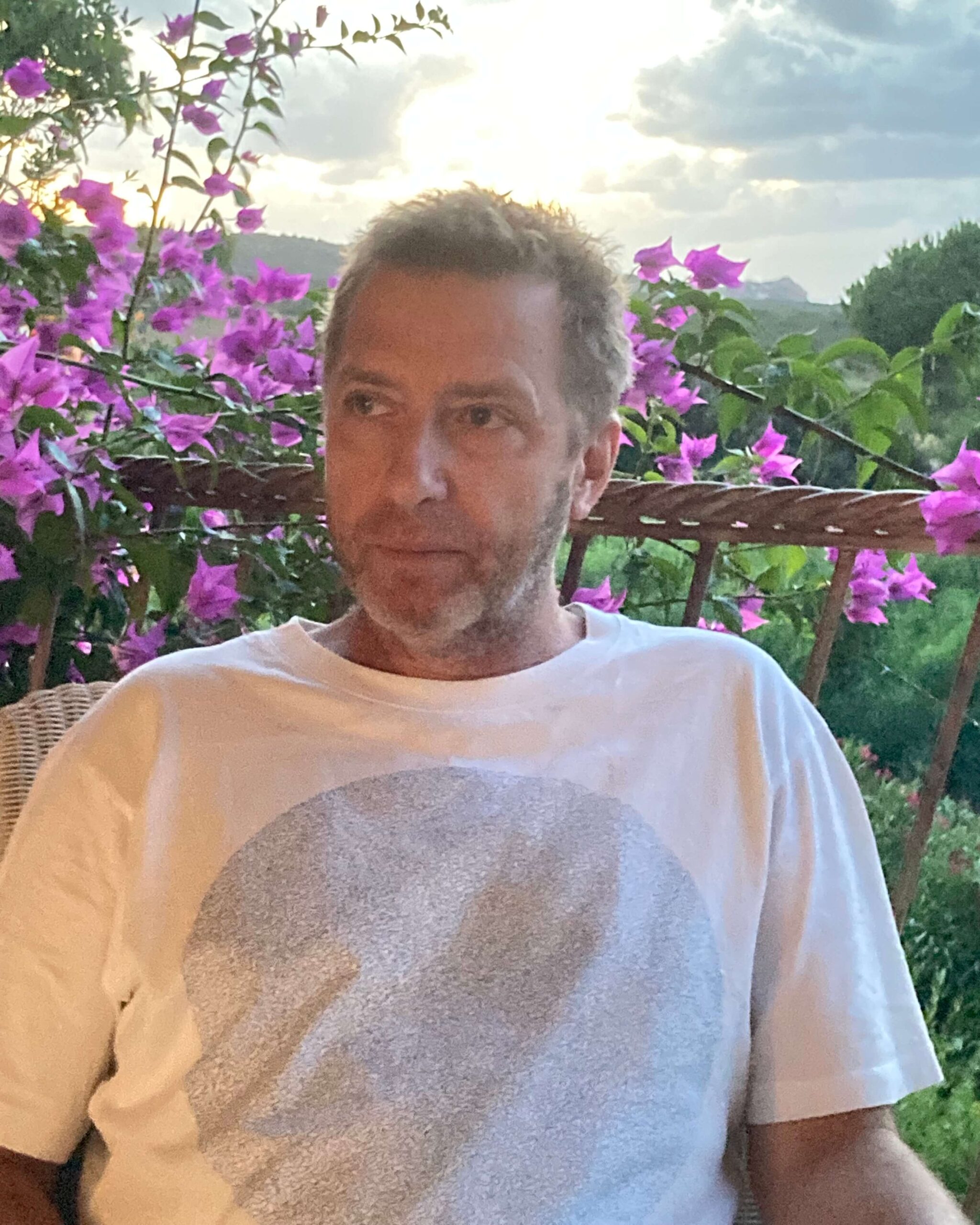Dr. Jeremy Narby in a white shirt sitting on a patio with purple flowers.