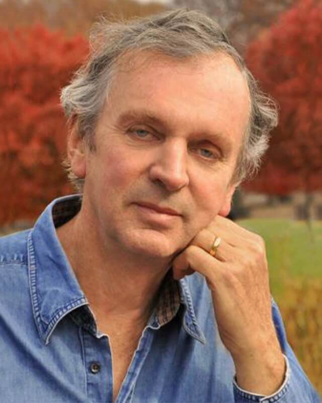 Dr. Rupert Sheldrake in a blue shirt leaning against a tree.