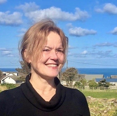 A woman standing in front of a field with the ocean in the background.